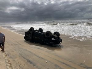 Photo of a black car that not only rolled, it was then swamped by the ocean.